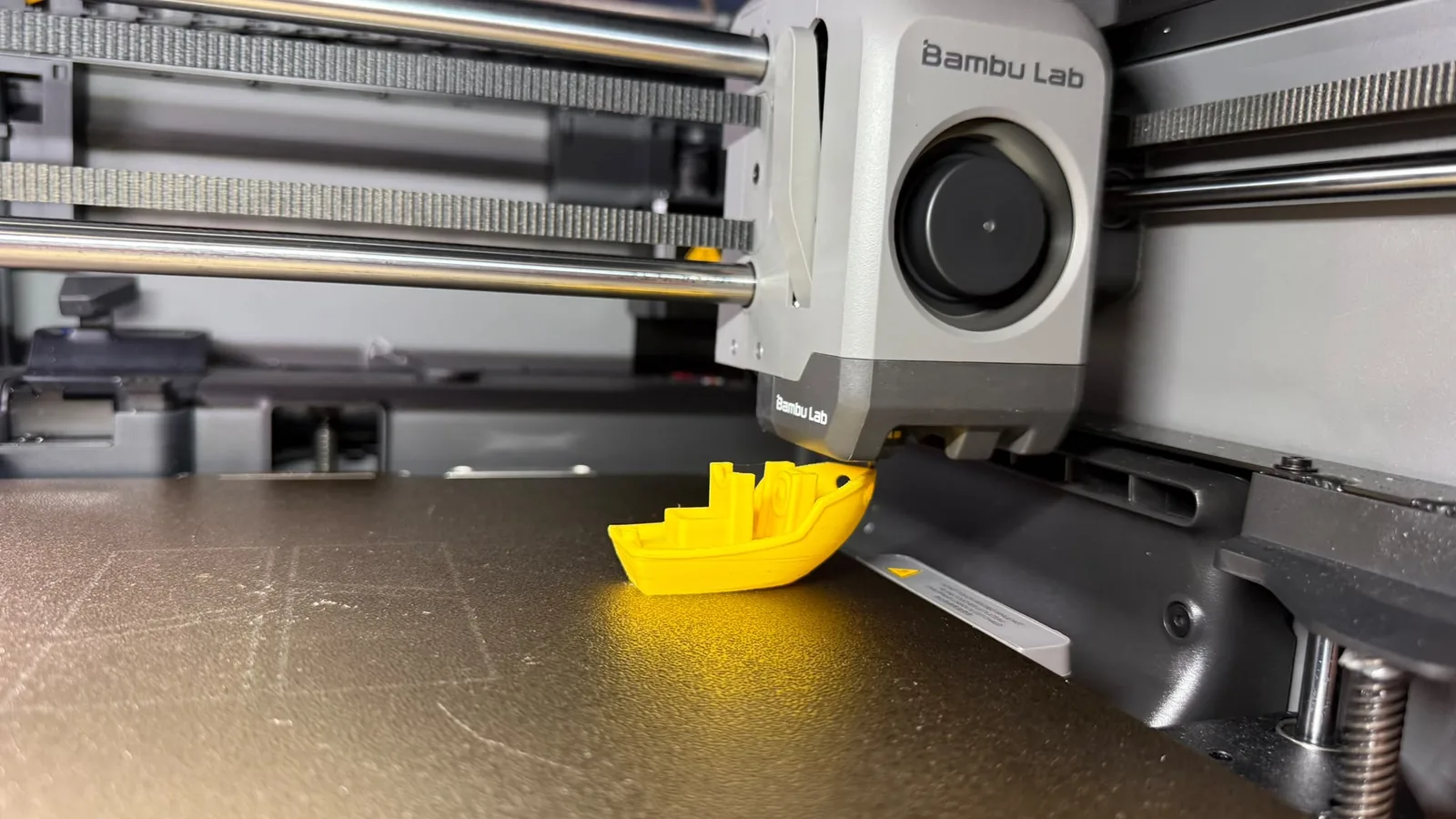 Testina Bambu Lab mentre stampa un Benchy giallo sul piatto di stampa